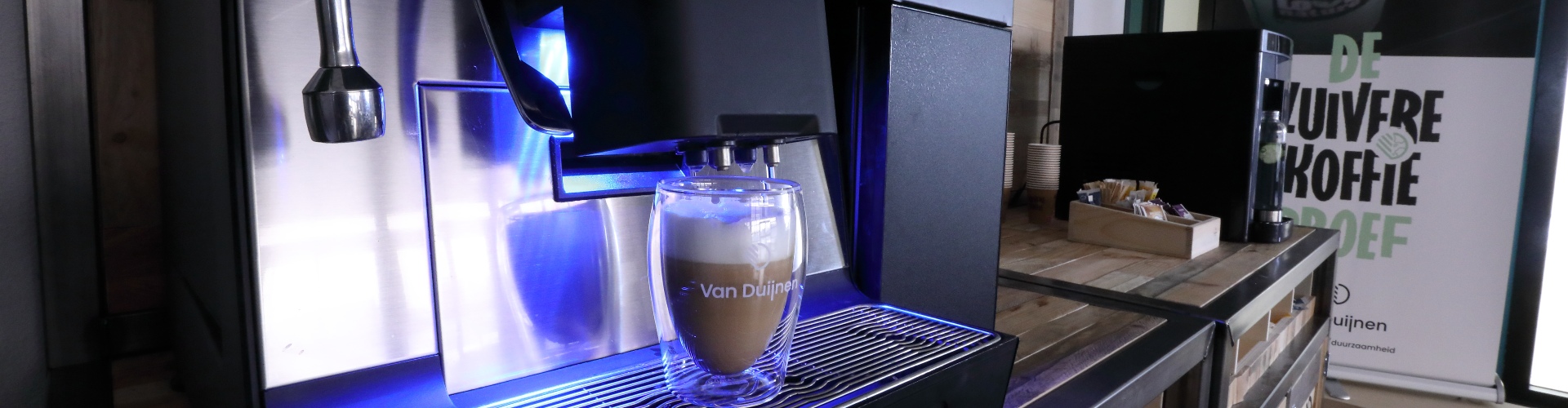 Koffie in theeglas met logo met cremalaag onder koffiemachine in koffiecorner